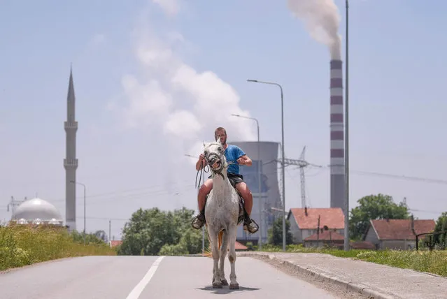 A man rides his horse next to Kosovo's coal-fired power plant near the town of Obilic on May 30, 2022. Two coal-fired power plants, Kosova A and Kosova B, are the main source of the alarming air pollution levels in Kosovo, and particularly in the town of Obilic, which is located between the two plants and near to their ash disposal sites and open-pit lignite mines. (Photo by Armend Nimani/AFP Photo)
