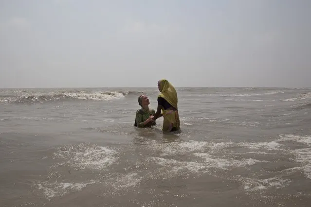 In this April 13, 2017 photo, a local woman helps Elizabeth Brenner, left, a mother from Minnesota, take a dip in the waters of Gangasagar in West Bengal, India, where the Ganges river flows into the ocean. Brenner was on a pilgrimage following the last footsteps of her son who died while studying abroad in India. She believes that part of her son's remains flowed across India through the Ganges river into the Bay of Bengal. (Photo by Rishabh R. Jain/AP Photo)