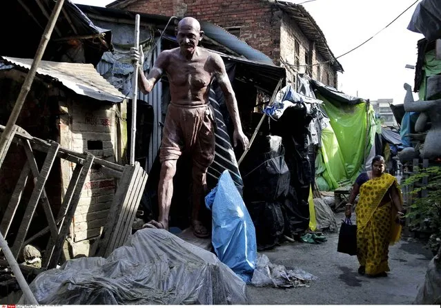 An Indian woman walks past a temporary structure and a huge statue of Mahatma Gandhi at Kumartuli in Kolkata, India, Saturday, August 8, 2015. Kumartuli or potters' place is where majority of clay sculptures of gods are produced in the city of Kolkata. (Photo by Bikas Das/AP Photo)