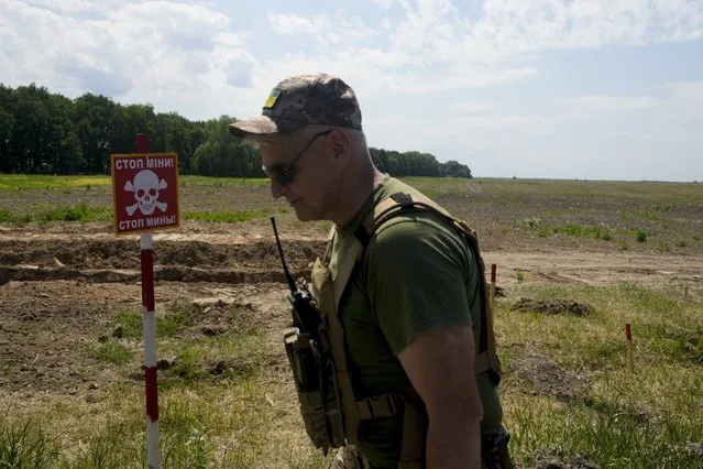 A Ukrainian soldier walks near a post warning about landmines in a field on the outskirts of Kyiv, Ukraine, Thursday, June 9, 2022. (Photo by Natacha Pisarenko/AP Photo)