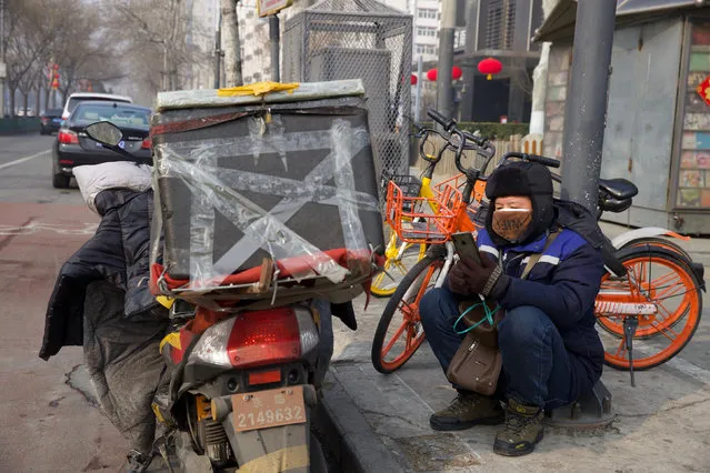 A deliver man uses his phone while waiting on a street of Beijing, China Tuesday, February 11, 2020. China's daily death toll from a new virus topped 100 for the first time and pushed the total past 1,000 dead, authorities said Tuesday after leader Xi Jinping visited a health center to rally public morale amid little sign the contagion is abating. (Photo by Ng Han Guan/AP Photo)