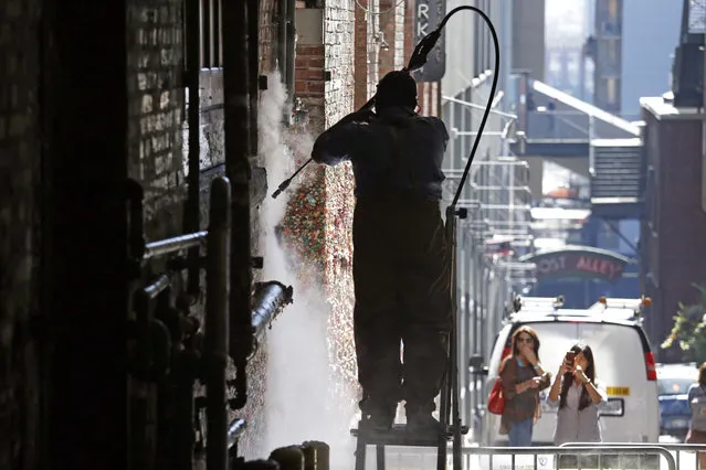 Two women look on as Leo Delgado sends up a cloud of steam as he pressure washes a year's worth of gum off of the landmark “gum wall” in Post Alley at the Pike Place Market Friday, September 15, 2017, in Seattle. (Photo by Elaine Thompson/AP Photo)