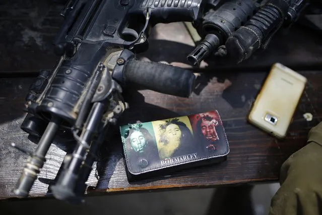 Israeli soldiers' weapons are placed beside a wallet with pictures depicting Reggae legend Bob Marley at Kibbutz Mefalsim near the border with Gaza August 28, 2014. An open-ended ceasefire in the Gaza war held on Wednesday as Prime Minister Benjamin Netanyahu faced strong criticism in Israel over a costly conflict with Palestinian militants in which no clear victor has emerged. (Photo by Amir Cohen/Reuters)