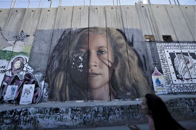 A tourist pauses in front of a mural depicting Palestinian activist Ahed Tamimi on Israel's controversial separation barrier in the West Bank city of Bethlehem, Sunday, June 19, 2022. (Photo by Maya Alleruzzo/AP Photo)
