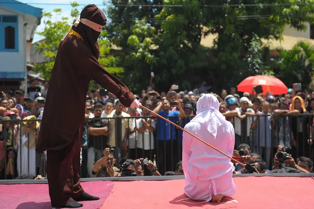 A religious officer canes an Acehnese youth onstage as punishment for dating outside of marriage, which is against sharia law, outside a mosque in Banda Aceh on August 1, 2016. The strictly Muslim province, Aceh has become increasingly conservative in recent years and is the only one in Indonesia implementing Sharia law. (Photo by Chaideer Mahyuddin/AFP Photo)