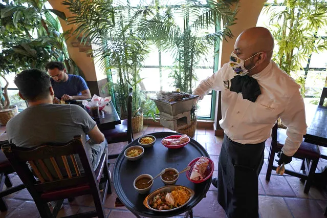 Waiter Marcos Huerta, right, serves a grill of fajitas at El Tiempo Cantina Friday, May 1, 2020, in Houston. The restaurant reopened their dining room for table service, with limited capacity, Friday. (Photo by David J. Phillip/AP Photo)