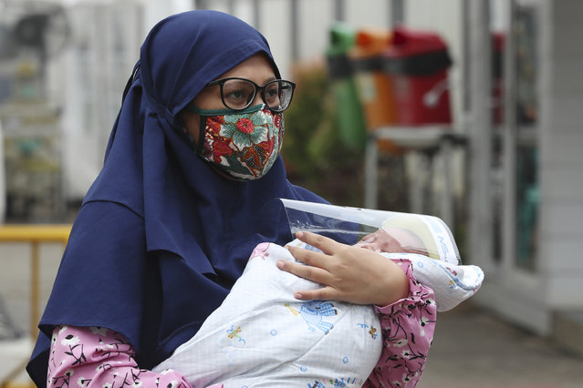 A Muslim woman carries her baby with face shield at a hospital in Jakarta, Indonesia, Tuesday, April 28, 2020. The world's Muslims have begun Ramadan with dawn-to-dusk fasting amid restrictions imposed to slow the pandemic that left many confined to their homes and public venues like parks, malls and even mosques are shuttered. (Photo by Achmad Ibrahim/AP Photo)