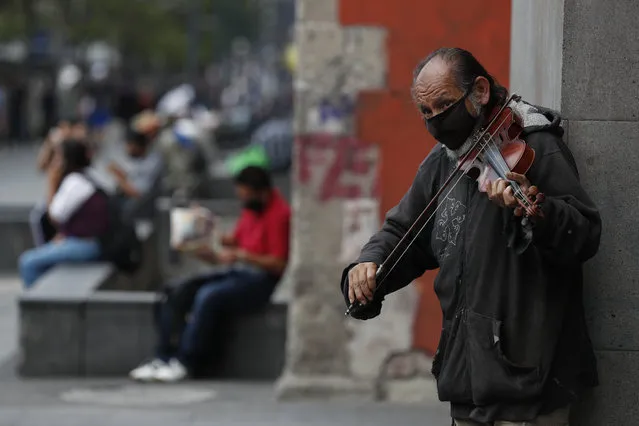 Fernando Castro, 59, plays a violin to earn tips from passerby, on Juarez Avenue in Mexico City, Sunday, May 31, 2020. Castro said he spent nearly two months at home before returning to busking in mid-May. “Necessity made me come out. I had no more money or food”, he said. “People have already begun to come back out. Curiously, many without face masks”. Mexico's capital plans to reopen certain sectors of the economy and public life beginning Monday, despite the city still being in the most serious “red light” phase of the coronavirus pandemic. (Photo by Rebecca Blackwell/AP Photo)