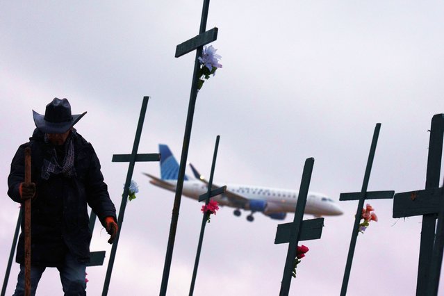 An airplane lands at Reagan National Airport as Roberto Marquez from Dallas, Texas, digs a hole for a cross as part of a memorial for the victims of the midair collision between an American Airlines plane and a military helicopter earlier this week in the Potomac River, Jan.31, 2025 in Arlington, Virginia. Flights have resumed in and out of Reagan National Airport after an American Airlines flight from Wichita, Kansas collided mid air with a military Black Hawk helicopter while on approach to the airport. According to reports, there were no survivors among the 67 people onboard both aircraft. (Photo by USA Today)