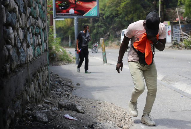 Men cover their airways as they walk near a barricade during a protest against insecurity, in Port-au-Prince, Haiti, on March 19, 2025. (Photo by Jean Feguens Regala/Reuters)
