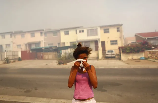 A girl wipes her eys as thick smoke engulfing homes in Ocean View, Cape Town, South Africa, 11 January 2016. Gale force South Easterly winds have been fanning several fires in the Cape making firefighting extremely difficult. The latest blaze ripped through the mountains above Scarborough and Misty cliffs as it moved towards Kommetjie narrowly missing the residential areas but now threatening Ocean View. Two hundred firefighters with 25 vehicles and five helicopters are on the scene fighting the blaze. (Photo by Nic Bothma/EPA/EFE)