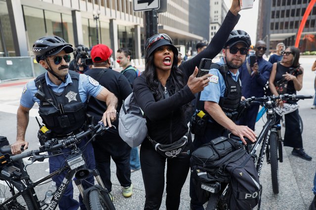 A woman holds a cellphone while she stands between two police officers during protest against federal immigration sweeps in Chicago, Illinois, on June 10, 2025. (Photo by Octavio Jones/Reuters)