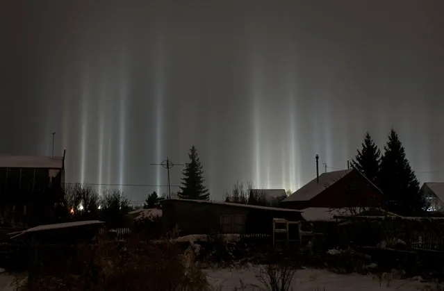 Pillars of light, which are optical atmospheric phenomena, beam up from the ground into the sky behind residential buildings in Omsk, Russia on January 2, 2023. (Photo by Alexey Malgavko/Reuters)