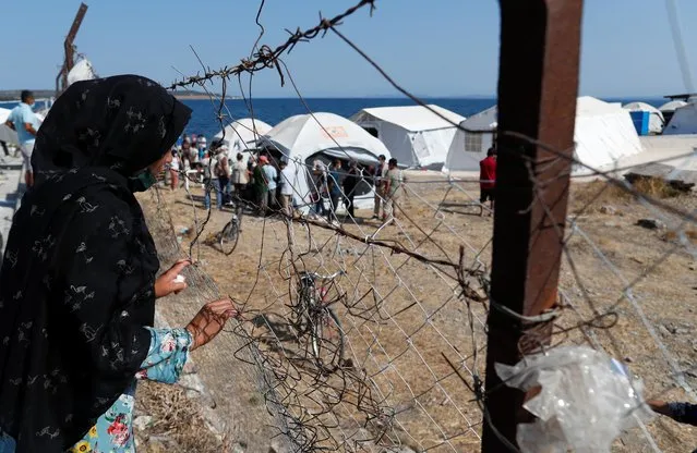 A woman looks through a chain-linked fence at a new temporary camp for migrants and refugees, on the island of Lesbos, Greece, September 22, 2020. (Photo by Yara Nardi/Reuters)