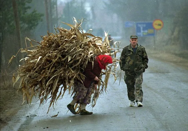In this Saturday, January 20, 1996 file photo, a Bosnian woman carries corn as a Bosnian soldier passes her in Lopare, a Bosnian former frontline village 10 kilometers (6 miles) north of Tuzla. (Photo by Karsten Thielker/AP Photo/File)