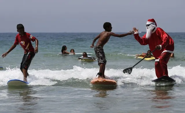 Carlos Bahia, dressed as Santa Claus, jokes with a child as they surf at the Maresias beach, in the state of Sao Paulo December 9, 2014. (Photo by Nacho Doce/Reuters)