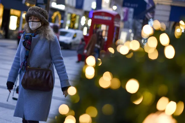 A woman wears a face mask as she walks past a Christmas tree in New Bond Street, in London, Tuesday, December 22, 2020. Britain's Prime Minister Boris Johnson cancelled Christmas for almost 18 million people across London and eastern and south-east England, following warnings from scientists of the rapid spread of the new variant of coronavirus. (Photo by Alberto Pezzali/AP Photo)