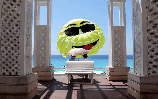 Two elderly people sit on a bench as they look at a happy face design on a parascending during a sunny day in Nice, France on June 1, 2018. (Photo by Eric Gaillard/Reuters)