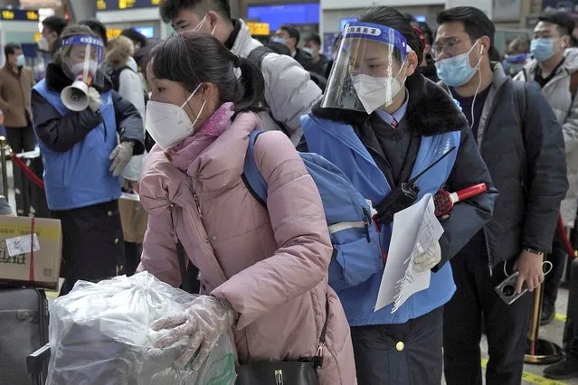Workers wearing face masks and face shields to help curb the spread of the coronavirus assist masked passengers to board their trains at the South Train Station in Beijing, Thursday, January 28, 2021. (Photo by Andy Wong/AP Photo)