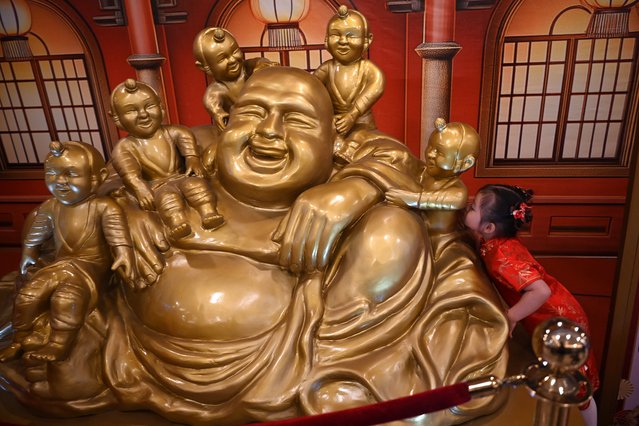 A young girl kisses one of the statues of a Buddha with children at a mall in Manila on January 24, 2025, ahead of the Lunar New Year of the Snake. (Photo by Ted Aljibe/AFP Photo) 