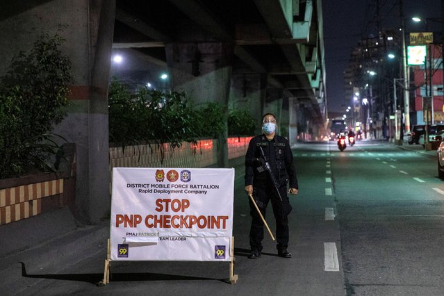 An armed police officer stands by a checkpoint placed to implement a curfew in the country's capital amid rising coronavirus disease (COVID-19) cases, in Caloocan City, Metro Manila, Philippines, March 16, 2021. (Photo by Eloisa Lopez/Reuters)