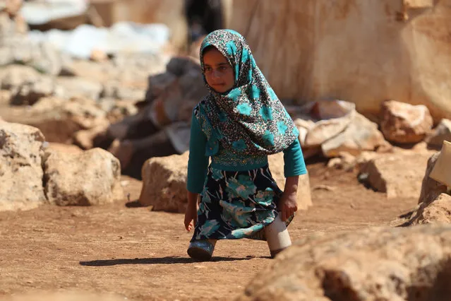 Eight year-old Maya Mohammad Ali Merhi walks using prosthetic legs made by her father from tin cans in a camp for displaced people, in the northern Syrian province of Idlib on June 20, 2018. Maya and her father were both born without lower limbs. Unable to afford real prosthetic limbs, her father made her a pair out of tin cans filled with cotton and scrap pieces of cloth. Maya's family had to leave their home in the Aleppo province to flee battles. (Photo by Aaref Watad/AFP Photo)