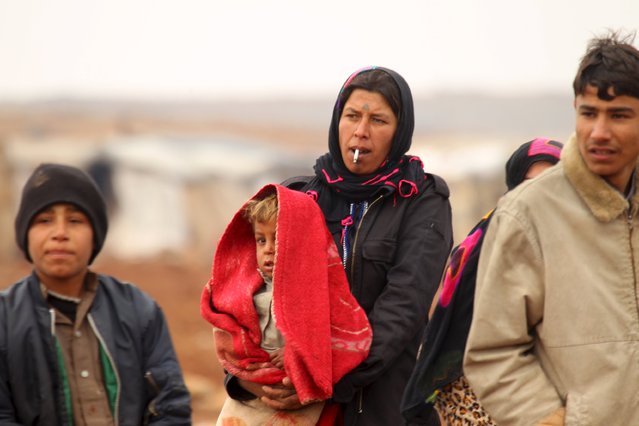 An Internally displaced Syrian woman carries a child while smoking a cigarette inside a refugee camp in the Hama countryside, Syria January 1, 2016. (Photo by Ammar Abdullah/Reuters)