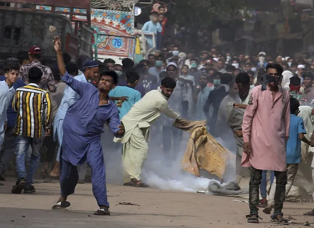 A supporter of Tehreek-e-Labiak Pakistan, a banned Islamist party, throws a stone while another tries to extinguish a tear gas canister fired by police to disperse protests over the arrest of their party leader Saad Rizvi, in Karachi, Pakistan, Monday, April 19, 2021. (Photo by Fareed Khan/AP Photo)