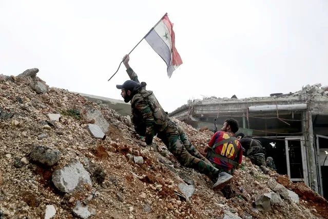 A Syrian army soldier places a Syrian national flag during a battle with rebel fighters at the Ramouseh front line, east of Aleppo, Syria, December 5, 2016. The fighting was most intense Monday near the dividing line between east and west Aleppo as government and allied troops push their way from the eastern flank. (Photo by Hassan Ammar/AP Photo)