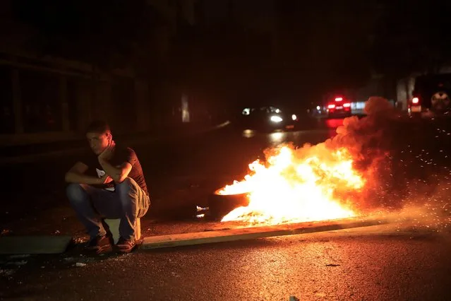 A protester sits next to burning tires, as he blocks a main street by burning tires, after a top court suspended a Central Bank decree that allowed the Lebanese to withdraw from dollar deposits at a rate two and a half times better than the fixed exchange rate, in downtown Beirut, Lebanon, early Thursday, June 3, 2021. In a late night burst of anger, dozens of protesters blocked main roads in Beirut and north of the capital to protest against the constant humiliation of Lebanese who line up to fill their cars with fuel, increasing power cuts, search for medicine and deal with confused banking decisions that are robbing thousands of their savings. (Photo by Hussein Malla/AP Photo)