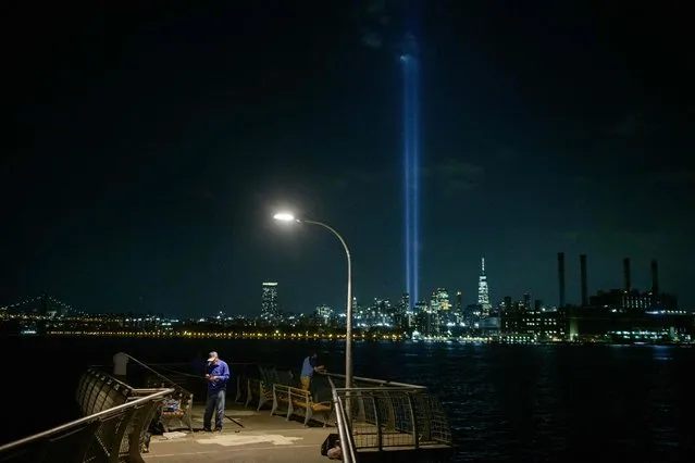A fisherman prepares his line on a pier before the “Tribute in Light” public art installation commemorating the 9/11 2001 terrorist attacks, shining up from the city skyline of lower Manhattan in preparation for the 20th anniversary, in Brooklyn, New York on September 7, 2021. (Photo by Ed Jones/AFP Photo)