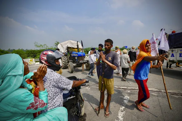 A farmer blocking traffic, center, refuses with folded hands as a woman on a motorcycle, left, requests for right of way at Singhu, outskirts of New Delhi, India, Monday, September 27, 2021. Thousands of Indian farmers Monday blocked traffic on major roads and railway tracks outside of the nation's capital, calling on the government to rescind agricultural laws that they say will shatter their livelihoods. The farmers called for a nation-wide strike to mark one year since the legislation was passed, marking a return to protests that began over a year ago. (Photo by Manish Swarup/AP Photo)
