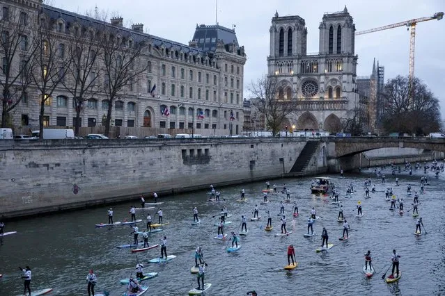 Competitors steer their Stand Up Paddle boards past Notre Dame cathedral during a race on the Seine river in Paris, Sunday, December 5, 2021. More than 1000 people took part to the competition though the French capital. (Photo by Adrienne Surprenant/AP Photo)