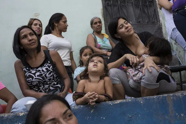 Women and their children watch mariachi musicians perform during a Mother's Day block party in Caracas, Venezuela, late Sunday, May 19, 2019. Although Mother's Day was officially celebrated the previous weekend, people in the Petare area organized the neighborhood party to celebrate the mothers of their community. (Photo by Rodrigo Abd/AP Photo)