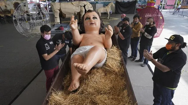 The Gomez Resendiz family applauds after placing a giant statue of Baby Jesus as preparations for Christmas celebrations, at the plaza of the Iztapalapa borough of Mexico City, Tuesday, December 21, 2021. (Photo by Marco Ugarte/AP Photo)