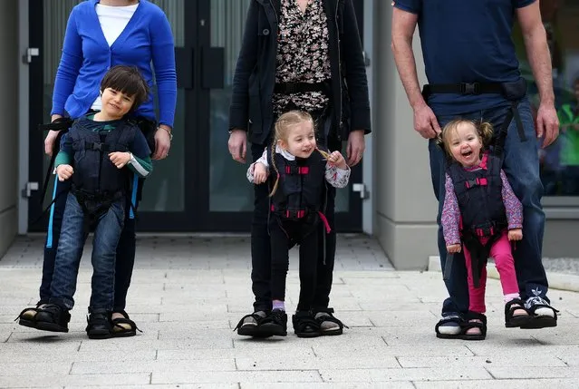 (Left to right) Daniel Smyth, 5, Bethany Watson, 3, and Charlotte Taylor, 3, using a Firefly Upsee, a new standing and walking harness for children with motor impairment, which attaches to a parent, allowing them and their child to take steps together, on March 24, 2014. (Photo by William Cherry/Presseye/PA Wire)