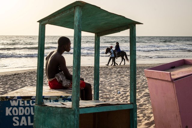A young man looks as a woman takes a horse ride along a beach in Banjul on May 4, 2024. (Photo by John Wessels/AFP Photo)