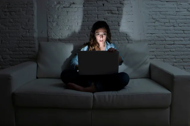 Young attractive woman at home sitting at living room sofa couch using laptop computer in dark evening light with intense face expression in internet and network addiction concept at night. (Photo by Marcos Calvo Mesa/Getty Images)