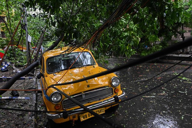 An uprooted tree is seen resting over a taxi after heavy rainfall in Kolkata on May 27, 2024, following the landfall of Cyclone Remal in India's West Bengal state. Residents of low-lying areas of Bangladesh and India surveyed the damage on May 27 as an intense cyclone that lashed the coast weakened into a heavy storm after killing at least three people, damaging homes and uprooting trees. (Photo by Dibyangshu Sarkar/AFP Photo)