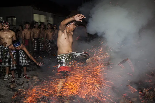 A Balinese man kicks up the fire during the sacred fire war ritual called “Mesabatan Api” ahead of Nyepi Day on March 27, 2017 in Gianyar, Bali, Indonesia. Mesabatan Api is held annually a day before the Nyepi Day of Silence , as it symbolizes the purification of universe and human body through fire. Nyepi, a day of silence, when Hindus on the island of Bali are not allowed to work, travel or take part in any indulgence. A fire war is performed by throwing fire of coconut fibers. In this game, boys will mingle and the players throw each other or attack each other. (Photo by Solo Imaji/Barcroft Images)