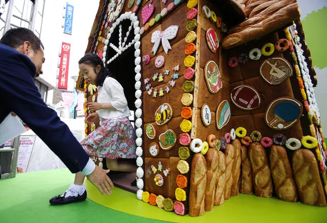 Six-year-old girl Nanami Miyazaki leaves a house made of sweets in Tokyo's Jiyugaoka district, Tuesday, May 3, 2016. The three-meter (10 feet)-tall house, made of a total of about 3,000 pieces of cakes, cookies, macarons and bread, stands in front of a station for the “Jiyugaoka Sweets Festa 2016” event to promote the town studded with many confectionaries during a three consecutive national holidays, Constitution Day on May 3, Greenery Day on May 4 and Children's Day on May 5. (Photo by Shizuo Kambayashi/AP Photo)