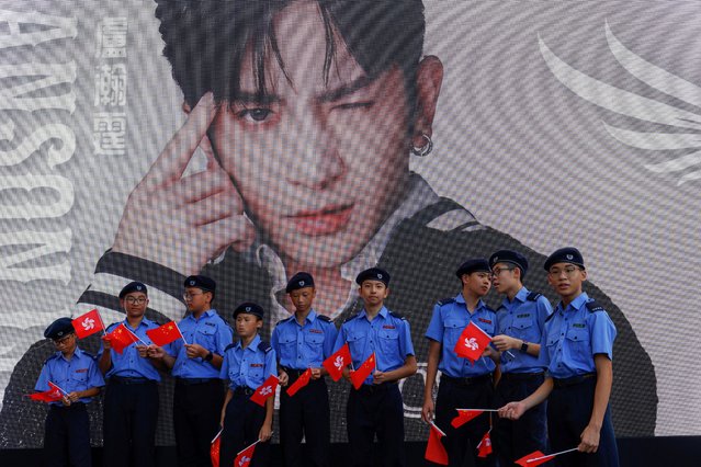 Members of a uniformed group holding Hong Kong and Chinese flags stand in front of a screen showing singer Anson Lo at an event celebrating the 27th anniversary of the former British colony's handover to Chinese rule in Hong Kong, China on July 1, 2024. (Photo by Tyrone Siu/Reuters)