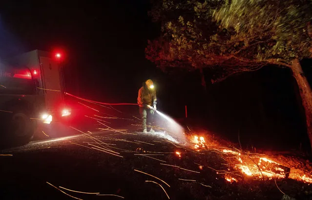 A firefighter battling the Kincade fire extinguishes a hot spot as strong winds send embers flying in Calistoga, Calif., on Tuesday, October 29, 2019. Millions of people have been without power for days as fire crews raced to contain two major wind-whipped blazes that have destroyed dozens of homes at both ends of the state: in Sonoma County wine country and in the hills of Los Angeles. (Photo by Noah Berger/AP Photo)