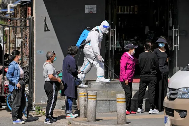 A worker in a protective suit sprays disinfectant as residents wearing face masks line up for mass coronavirus testing outside a residential complex, Tuesday, May 3, 2022, in Beijing. (Photo by Andy Wong/AP Photo)