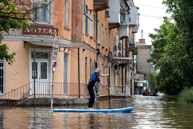 A local resident sails on a sup board during an evacuation from a flooded area in Kherson on June 8, 2023, following damages sustained at Kakhovka hydroelectric power plant dam. Ukrainian President Volodymyr Zelensky visited the region flooded by the breached Kakhovka dam Thursday, as the regional governor said 600 square kilometres were underwater. (Photo by Aleksey Filippov/AFP Photo)