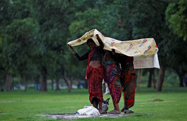Women use a plastic sheet to cover themselves from rain at the India Gate lawns in New Delhi, June 28, 2017. (Photo by Adnan Abidi/Reuters)