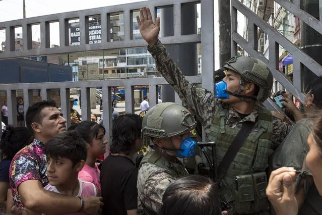 A soldier tries to organize people waiting to enter Gamarra clothing and textile market in Lima, Peru, Monday, March 16, 2020. Peruvian President Martin Vizcarra has declared a state of emergency, ordering citizens to stay in their homes and temporarily suspending certain constitutional rights, to contain the spread of coronavirus. According to the World Health Organization, most people recover in about two to six weeks from the new coronavirus, depending on the severity of the illness. (Photo by Rodrigo Abd/AP Photo)