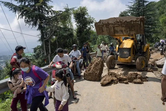 People rush past an earthmover clearing a road of a big rock that came down with mud and plant debris following intense monsoon rains in Dharmsala, Himachal Pradesh state, India, Sunday, August 21, 2022. Landslides and flooding over the last three days killed at least three dozen people in this Himalayan state, an official government release said Sunday. (Photo by Ashwini Bhatia/AP Photo)