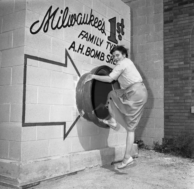 Mrs. Marie Graskamp of Milwaukee shows the different positions one might assume when entering the bomb shelter in Milwaukee  September 3, 1958. This circular entrance is about three feet in diameter. This is the entrance (according to the builders) that would connect to the cellar of a home assuming the shelter was in the ground for added protection. (Photo by AP Photo)