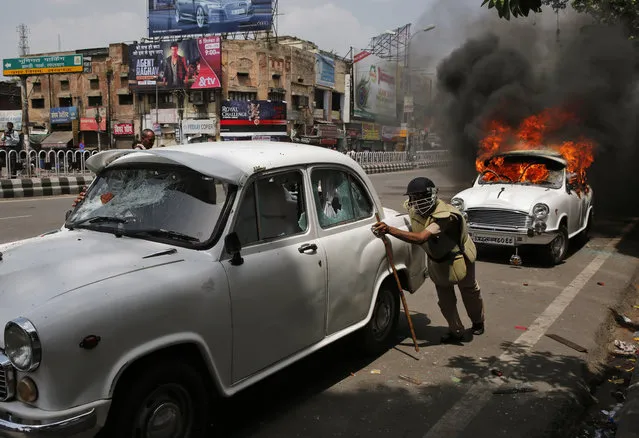 An Indian policeman pushes government car as another stands in flames after it was set on fire by students of Bachelor of Physical Education during a protest in Lucknow, India, Tuesday, September 1, 2015. Police used batons and water canons to disperse protesters near the legislative assembly as they resorted to stoning. The students were demanding the state government to allot permanent jobs to them. (Photo by Rajesh Kumar Singh/AP Photo)